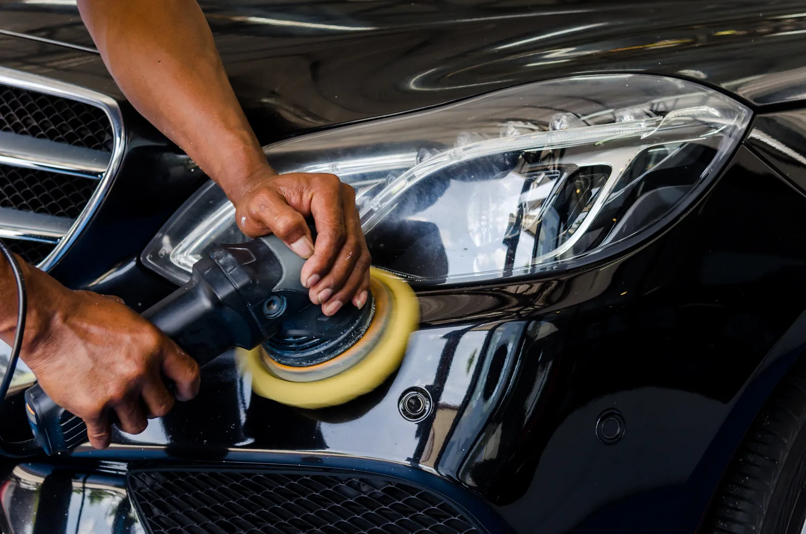 Hands polishing a car with an orbital polisher during detailing